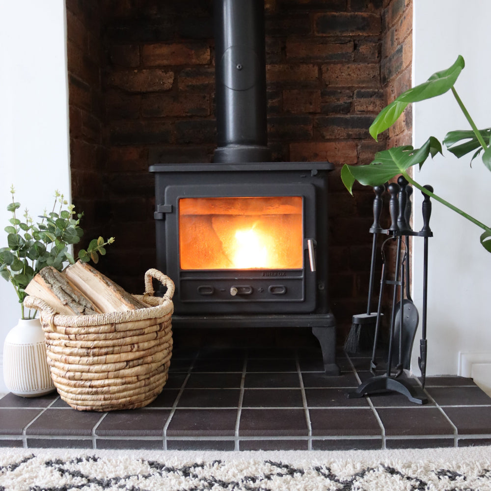 Log Burner with fire inside and basket of kiln-dried logs next to it