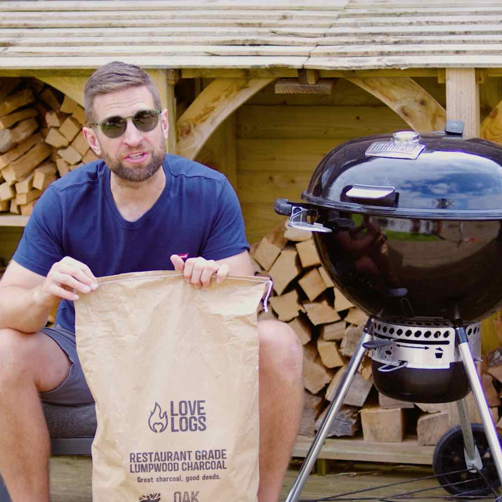 Paul from Love Logs sat next to a kettle BBQ holding a bag of charcoal