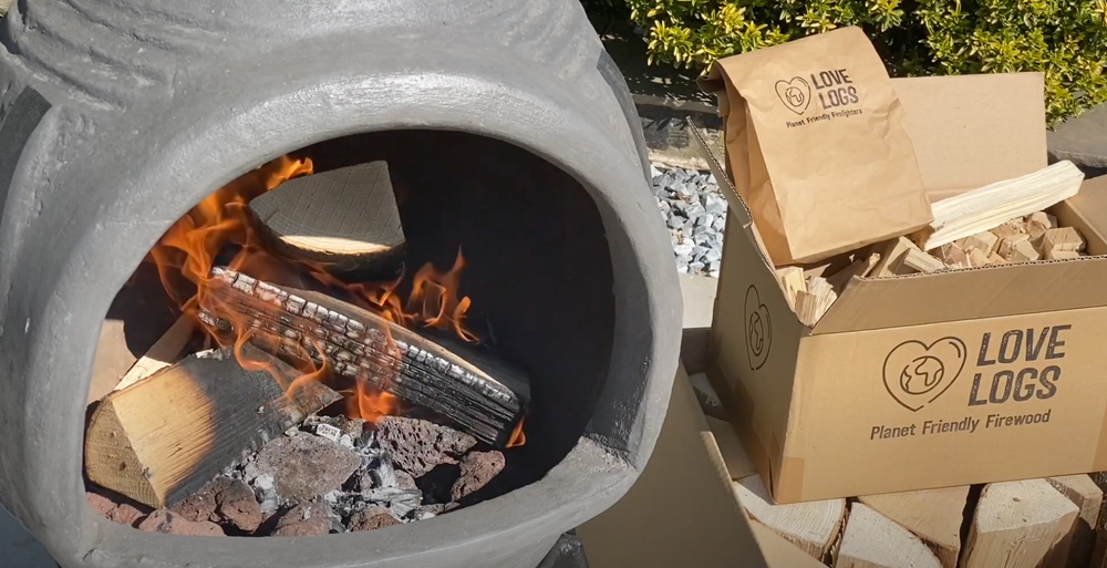 Clay chiminea with a fire burning inside it, next to a Love Logs box