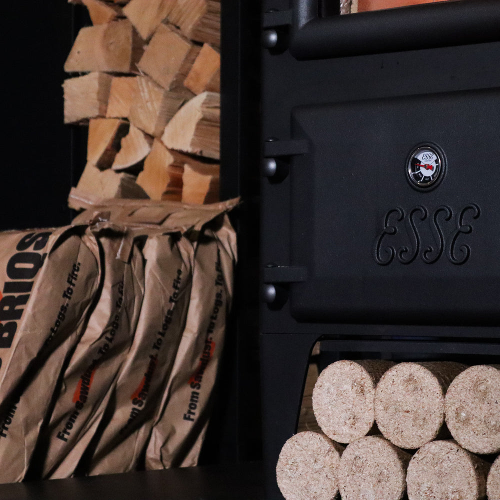 
                      
                        Bio Briqs firewood briquettes stackked in bags nest to log burner
                      
                    